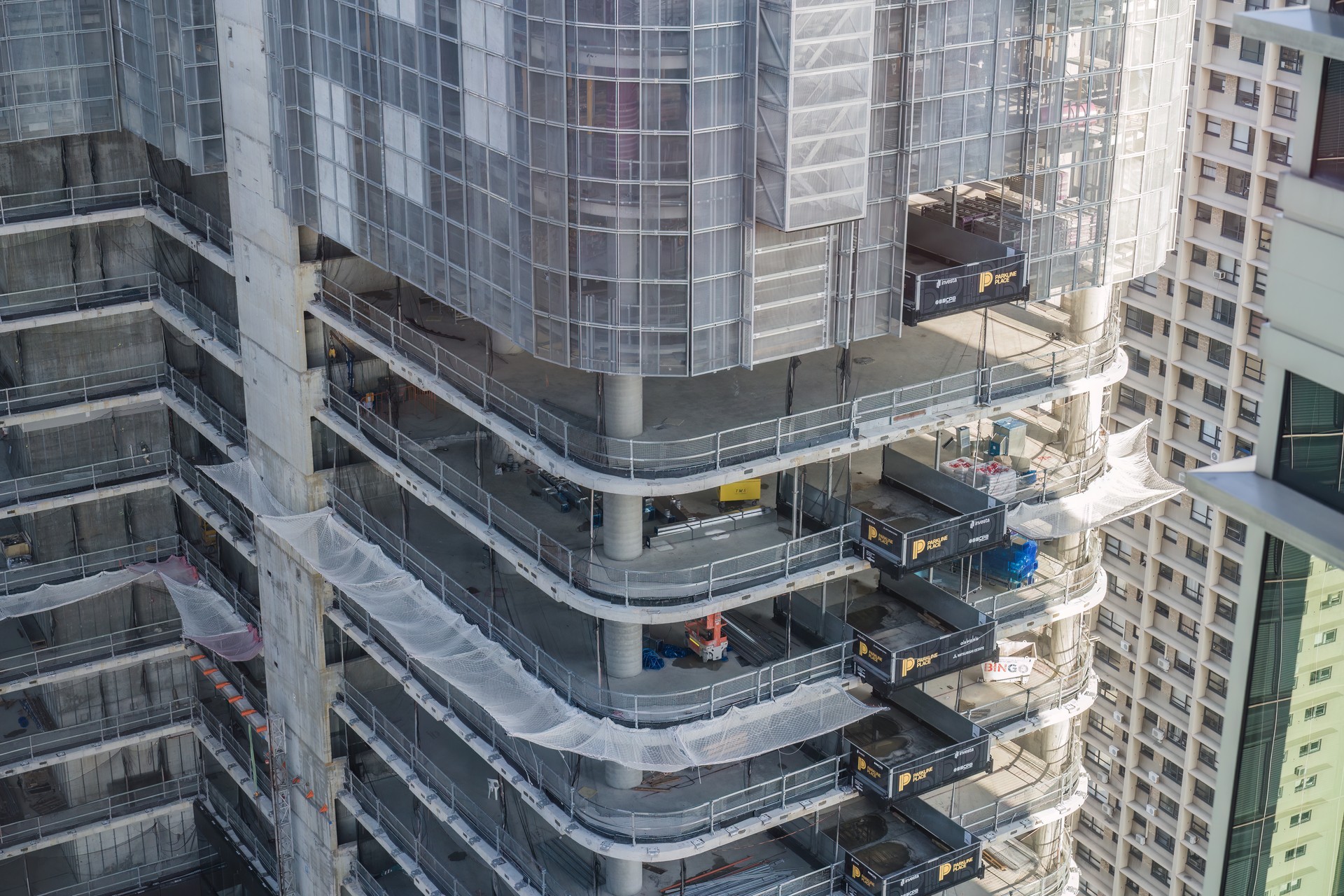 Un edificio de gran altura en construcción que muestra pisos de concreto a la vista y andamios cubiertos